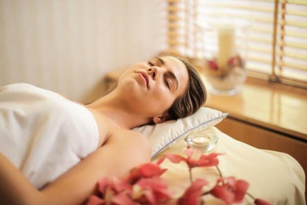 A woman lying on her back with eyes closed, candle and flowers nearby