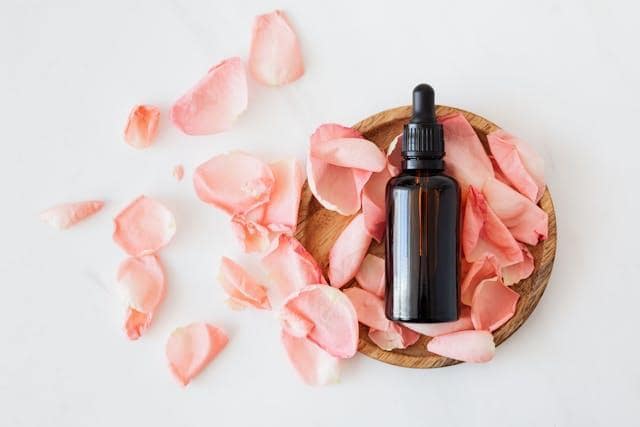 A small bottle and rose petals in a wooden bowl.