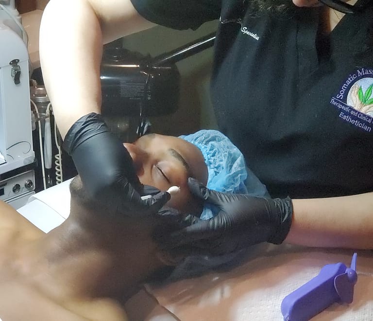 man laying on table with esthetician applying a solution to his face