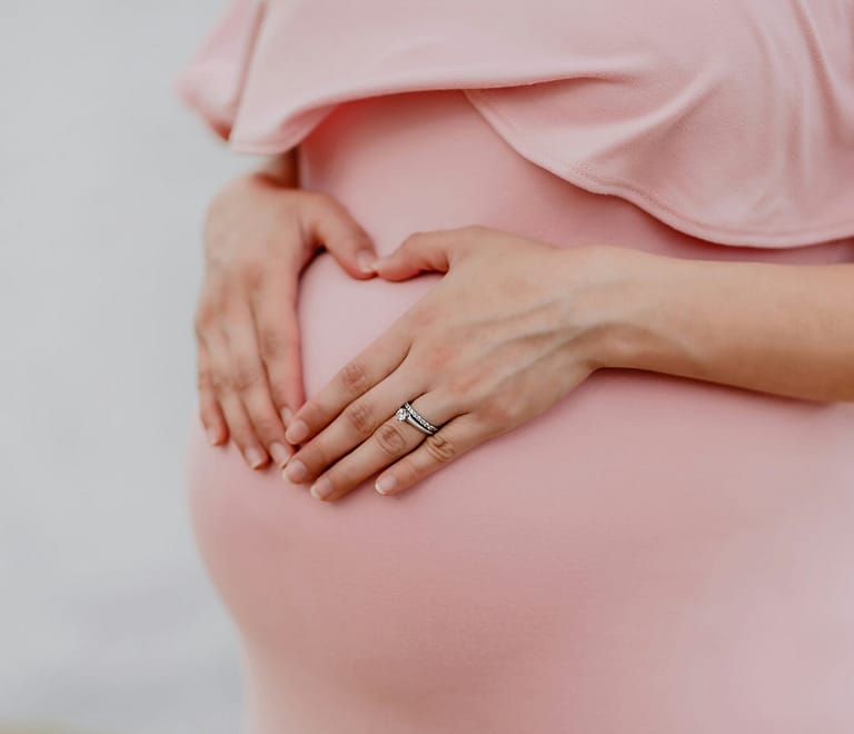 Expecting mother in a pink dress holds her stomach preparing for a prenatal massage