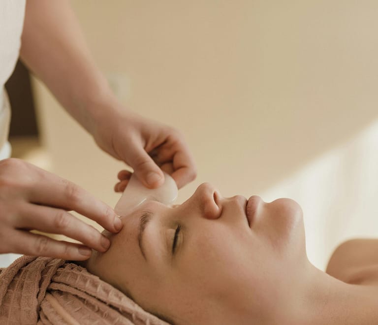 An aesthetician uses gua sha tools on the face of a customer who is laying down on a massage table
