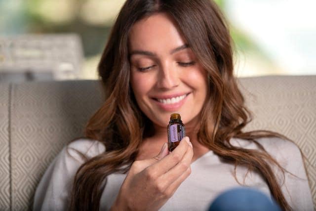 A woman smiling while inhaling essential oil from a small bottle.