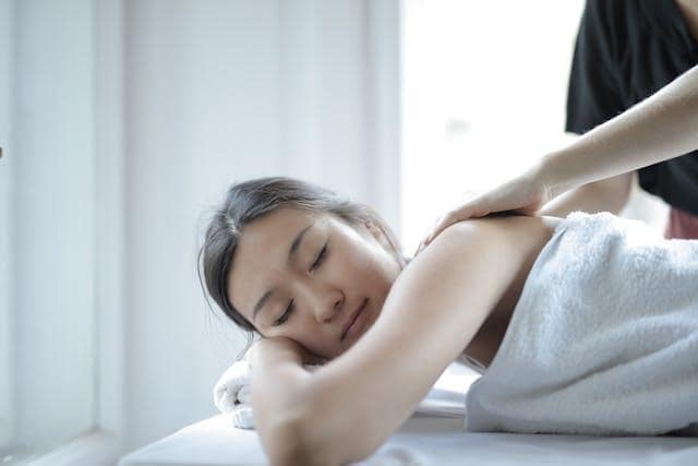 A woman sleeping while getting a massage on a white towel.